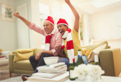 Enthusiastic mature couple in matching hats and scarves cheering watching TV sports event